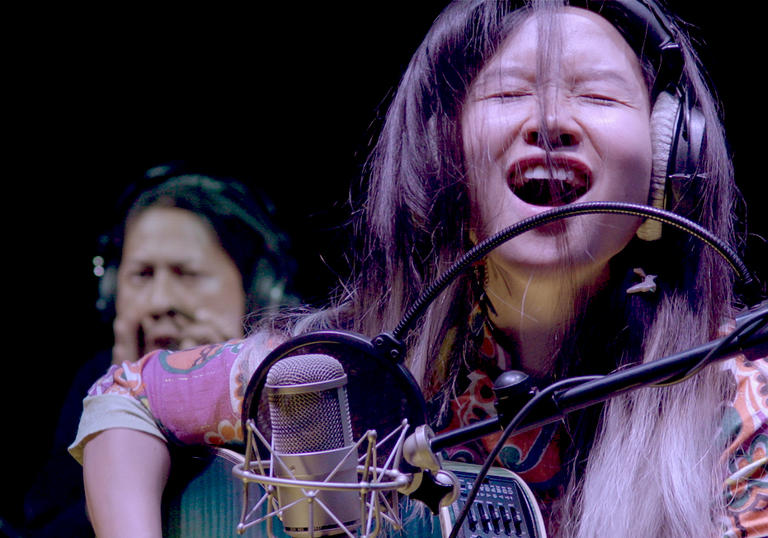 A woman singing into a microphone and playing a guitar