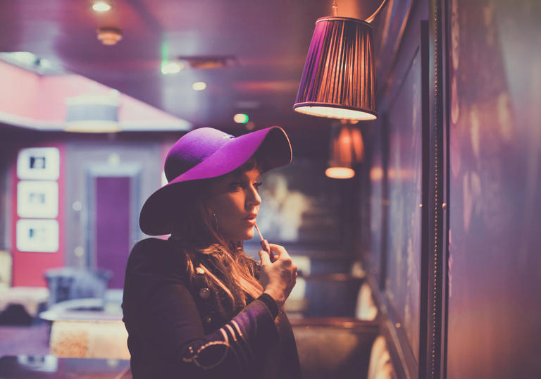 Natalie Williams wearing a fetching purple hat putting make-up on in the mirror