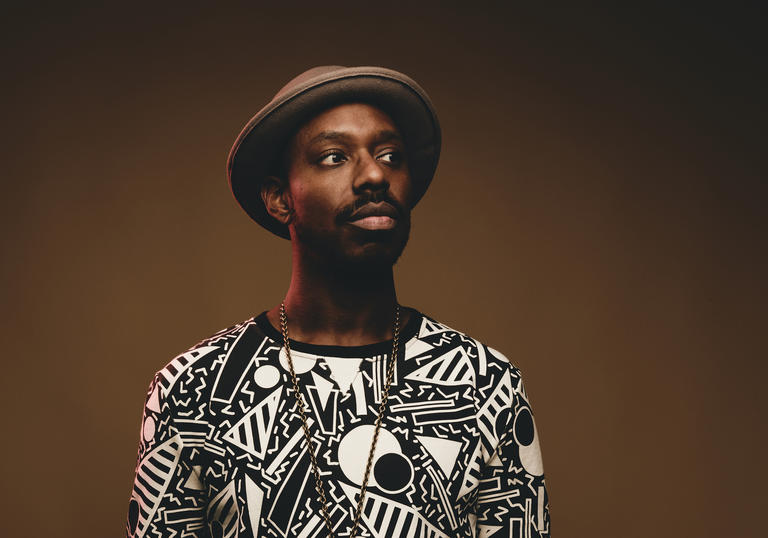 Shabaka Hutchings wearing a patterned top and hat, looking to his left.