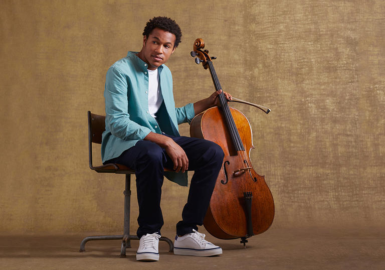 Sheku sitting on a chair holding his cello 