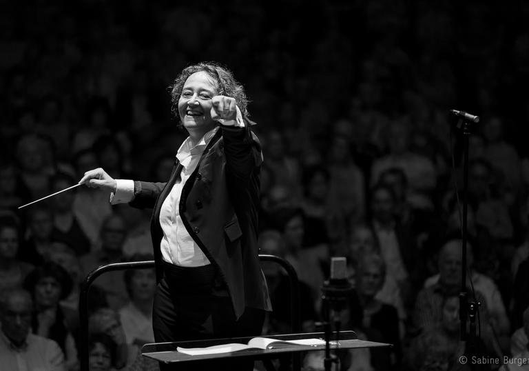 An image of Nathalie pointing at the camera joyfully whilst conducting in a recent concert