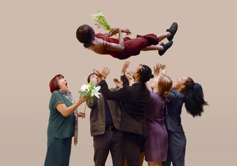Five people launch a person into the air, as she holds a flower bouquet