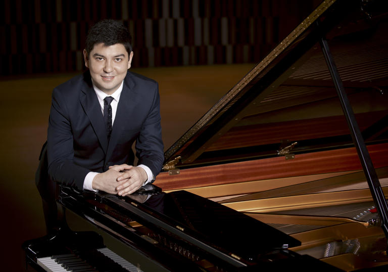 Behzod leaning on a piano happily