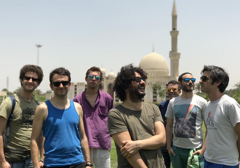 Sofiane Saidi & Mazalda standing in front of a mosque, wearing sunglasses in the sunshine