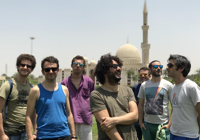 Sofiane Saidi & Mazalda standing in front of a mosque, wearing sunglasses in the sunshine