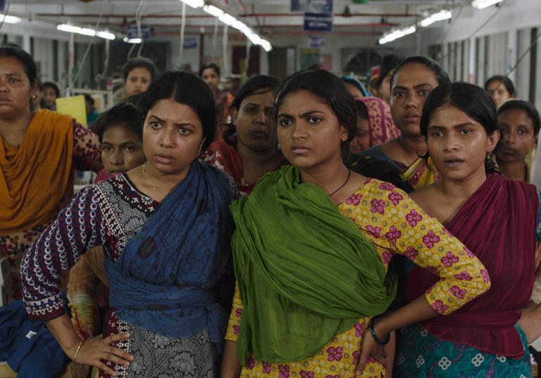 A group of Bangladeshi women inside a factory gather together to look at something off camera
