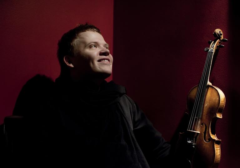 Pekka smiling joyfully as he gazes into the middle distance, violin in hand