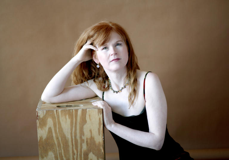A portrait of Sarah leaning on a wooden plinth