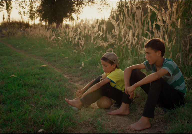 two kids sitting in a field with long grass behind them