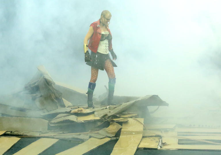 French artist Phia Ménard, who plays Athena stands atop a destroyed cardboard structure surrounded by smoke. Photo by Jean-Luc Beaujault