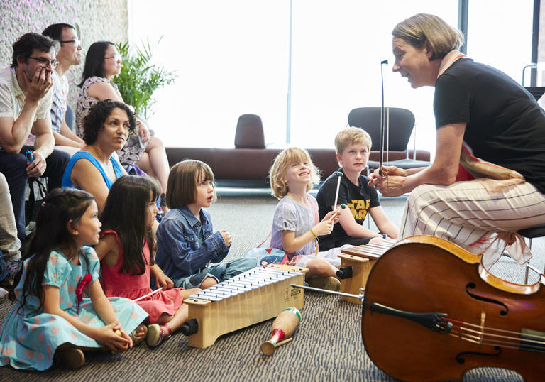 A Member of the LSO talks to a group of children. The have a cello and percussion instrumnets to try.