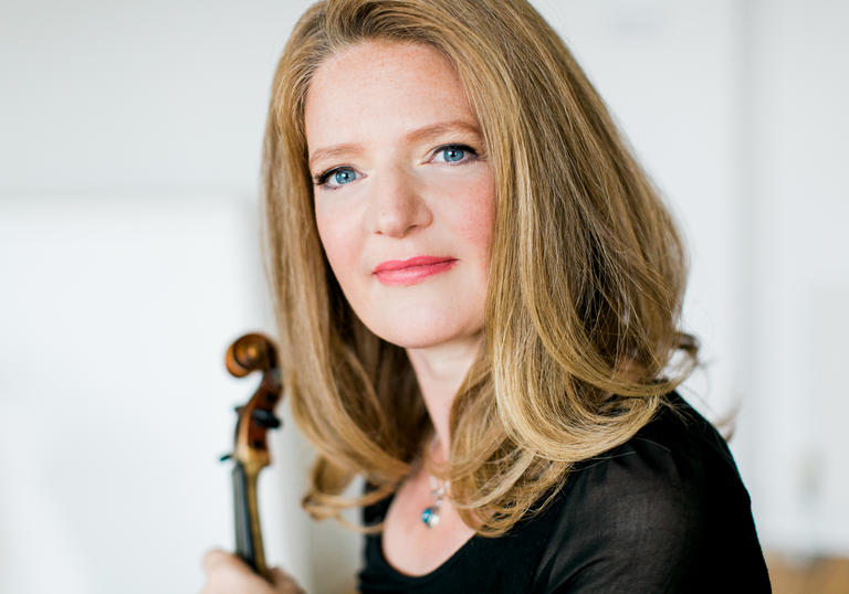 A portrait Rachel Podger, violin in hand, her blue eyes glistening