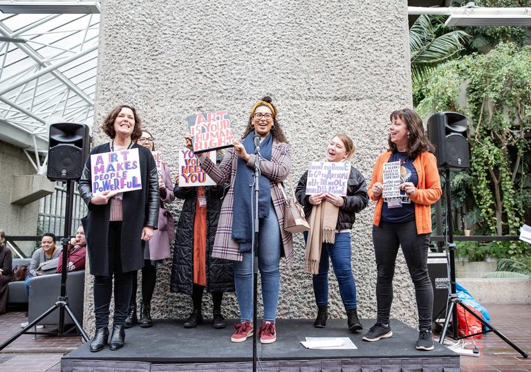 Group of woman on a stage holding up painted cards which say teaching is beautfiul