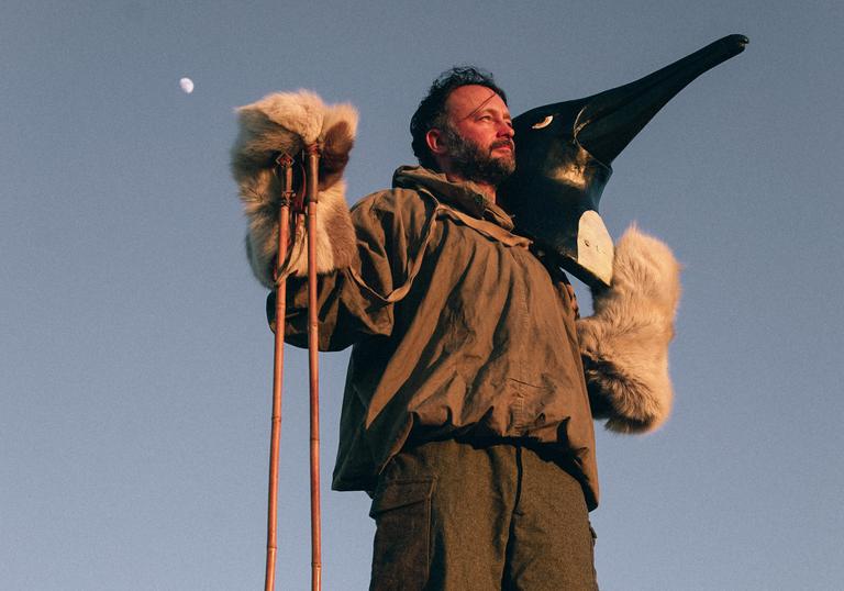 Arthur Jeffes standing with a walking stick and holding a fake penguin head on his shoulder