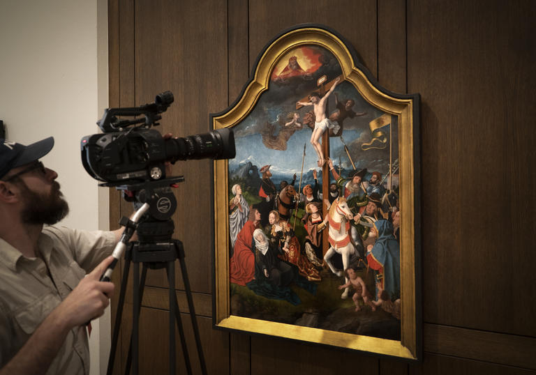 A man films a painting depicting the crucifixion of Jesus Christ