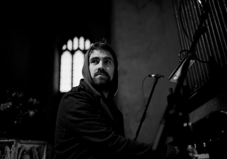 black and white image of Kit Downes playing the organ with an arched church window in the background