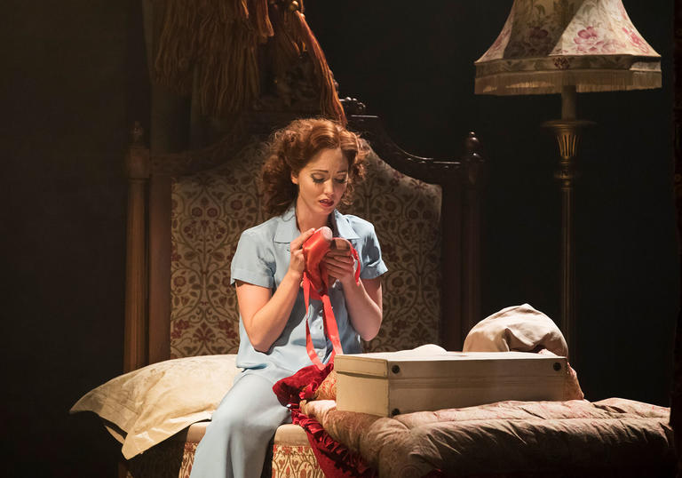 lady sitting on the bed looking at her red ballet shoes