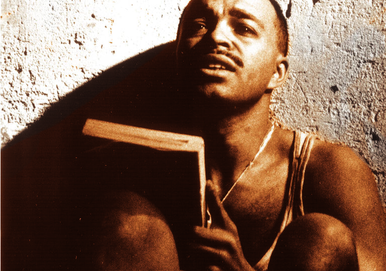 A man sat against a wall holding a book