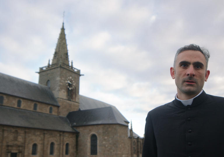 A priest stands next to a church