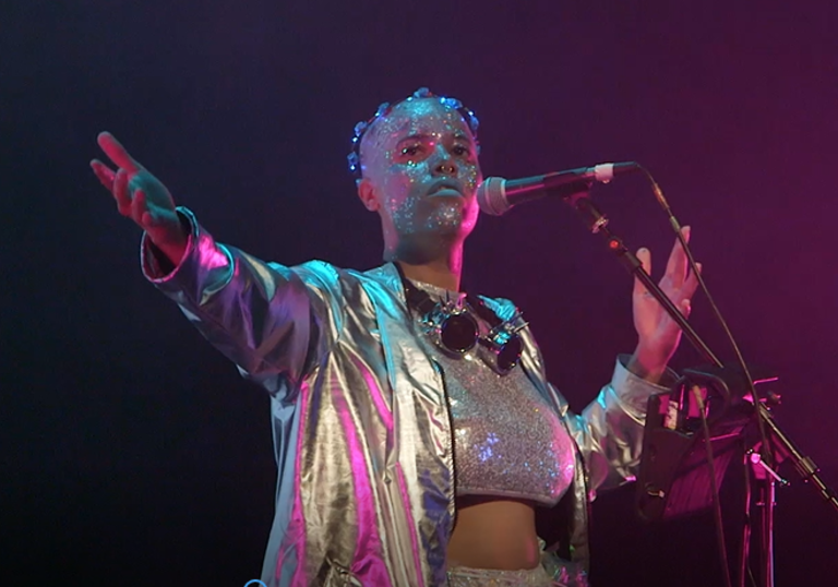 photo of a performer wearing glitter and holding a microphone