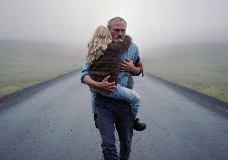 A man carrying a young girl along a deserted road