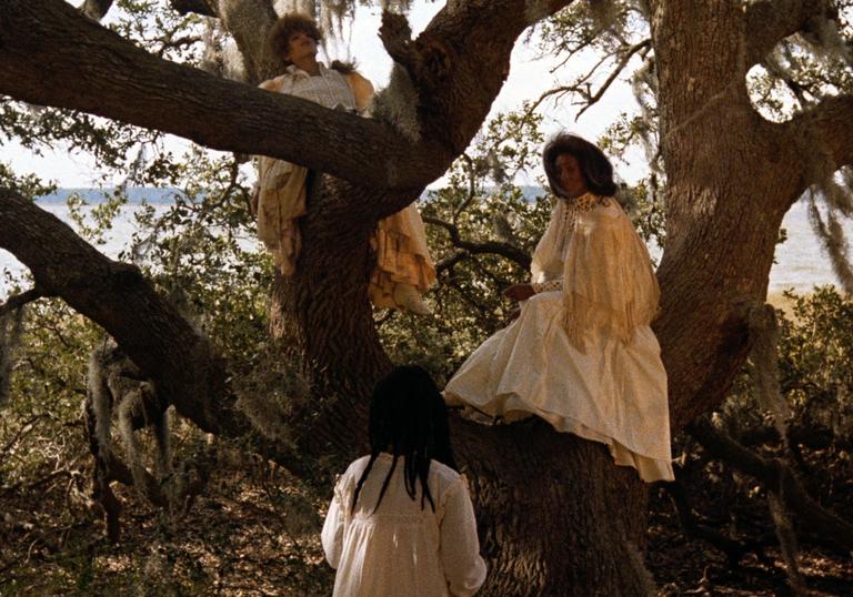 two women wearing white gowns next to big trees