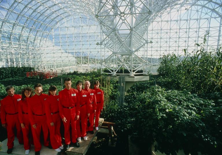 people in red boiler suits standing in a massive green house