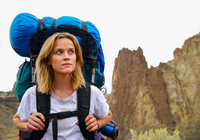reese witherspoon with hiking bags in the middle of some mountains