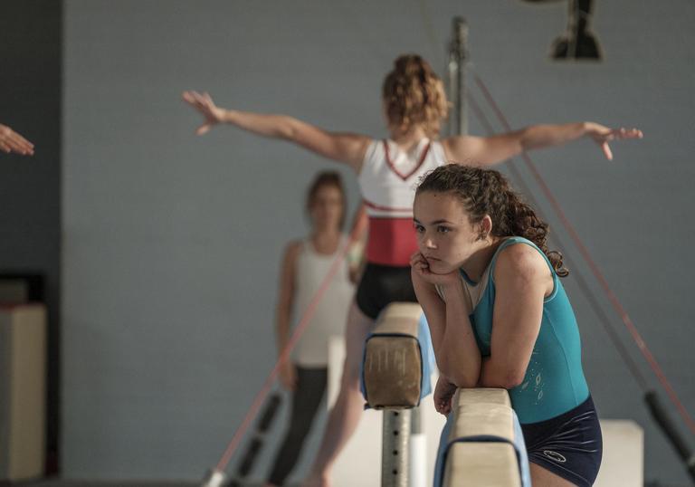 young girl leans on a balance bar with a gymnastics studio 