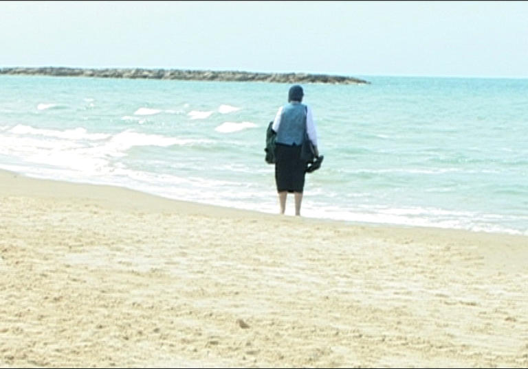 a lone figure on a beach looking out at a very blue ocean