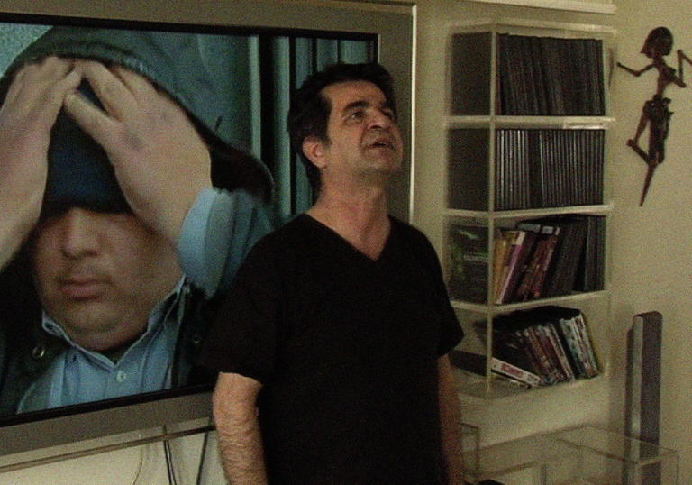 a man stands in a house with an image behind him, the image is of a man with his head in his hands