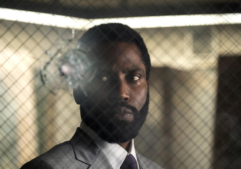 A close up of John David Washington behind glass with criss-cross wiring and a bullet hole