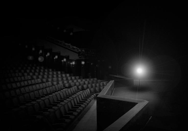 An empty Barbican Theatre lit with just a single white light on a stand stood on an empty stage.