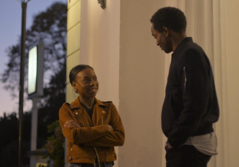 two young people stand opposite each other talking at dusk