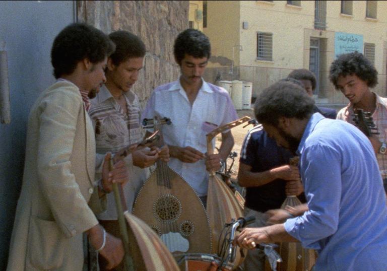 A group of men gather round some instruments on the street in bright sunlight