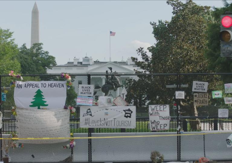 lots of signs tied to a fence in front of Washington DC landmark