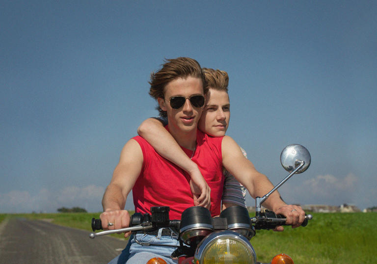 two boys on a motorbike with blue sky behind them