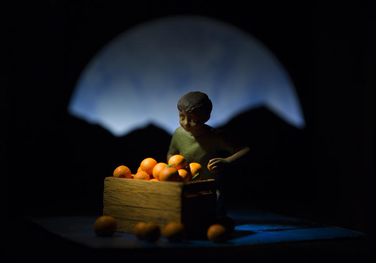 Photo of a boy sitting by a box of oranges