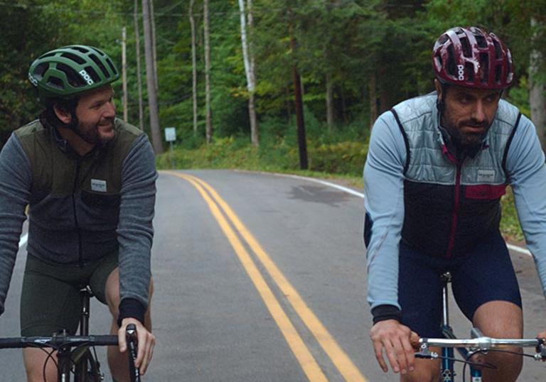 two men cycling on a road side by side