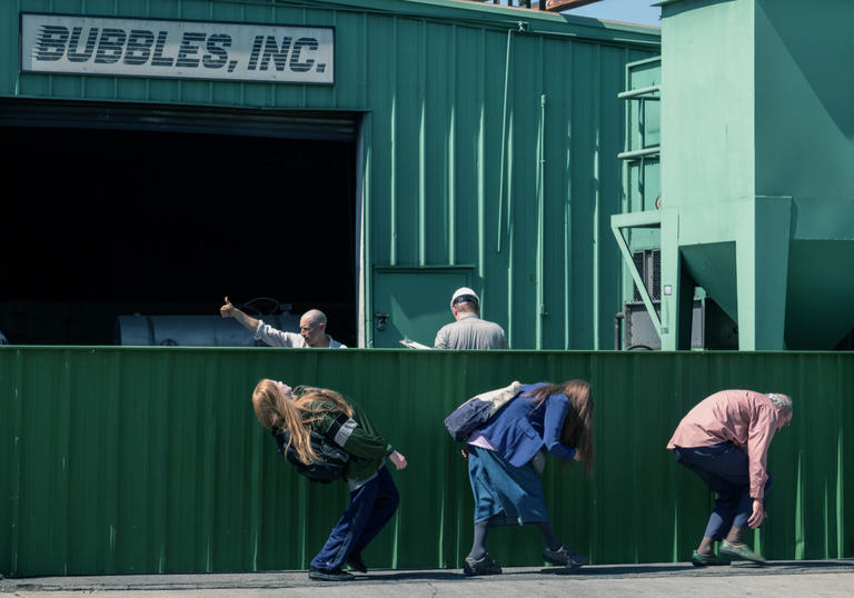 a man an two women hunch down so they can't be seen walking past a fence