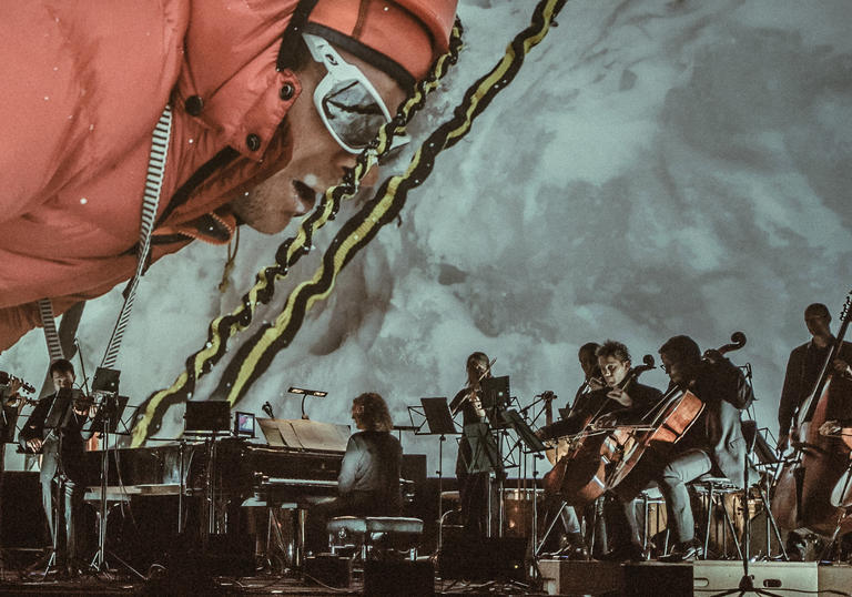 Image of the ACO playing in front of the film Mountain featuring a climber in goggles up a mountain