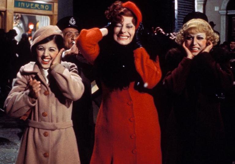 three women wearing big coats and giggling in the street