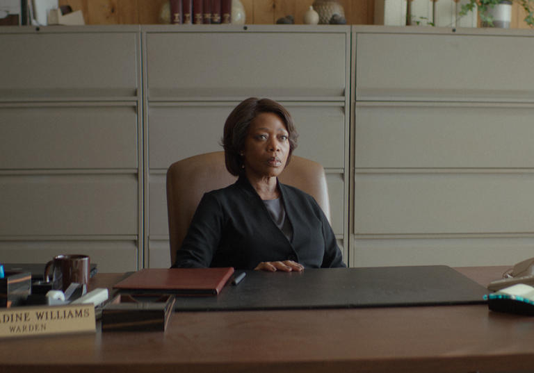 Alfre Woodard sits behind a big desk wearing a suit