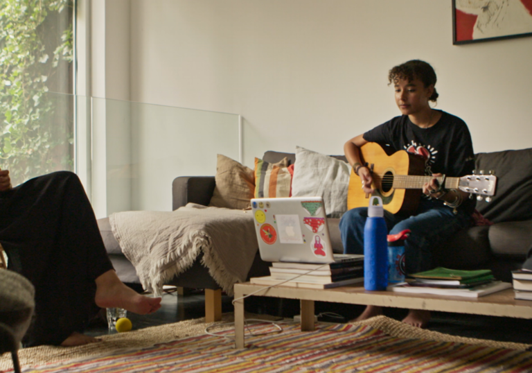 two women sit across from each other in a room, one holding a guitar