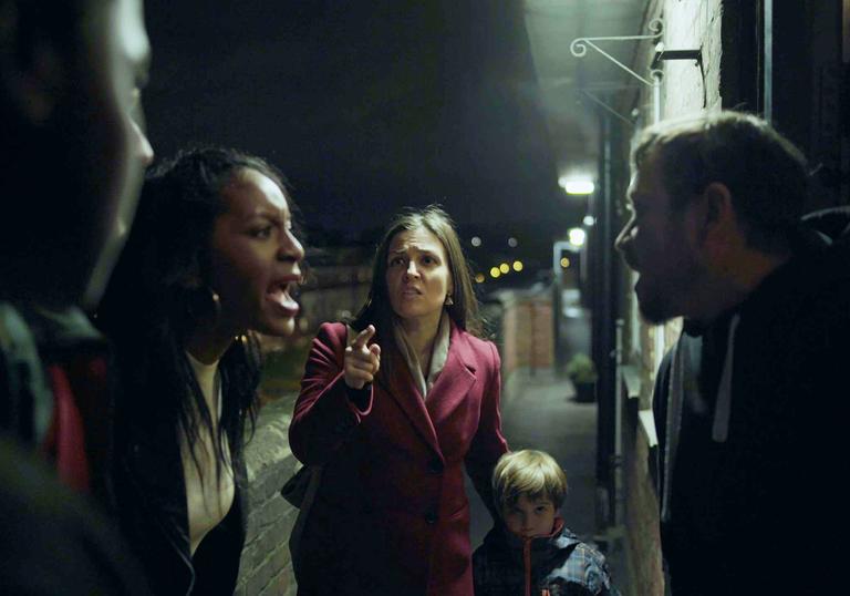 a group of people argue on a walkway outside a block of flats