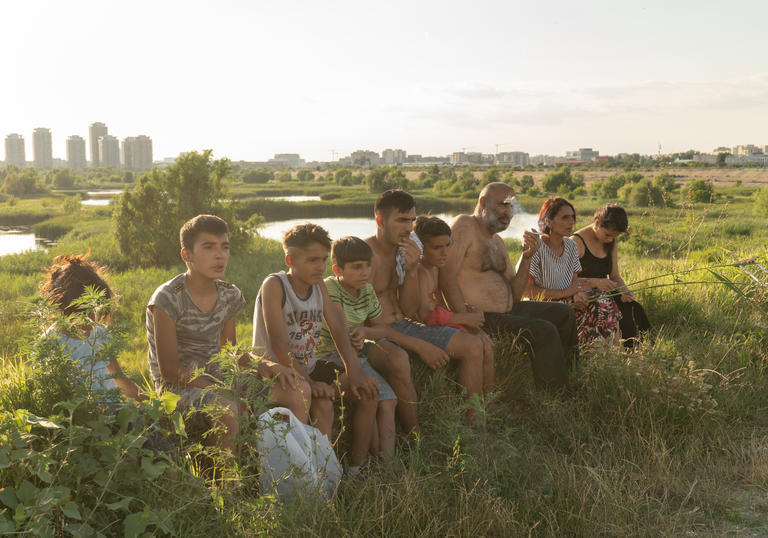 A family sit in a row surrounded by a green field, with a city visible in the distance