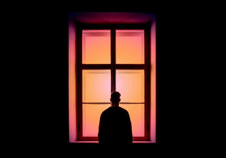 Silhouette of man looking out of a pink window