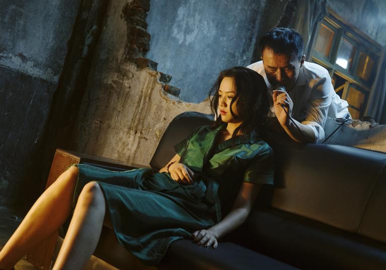 a woman in a green dress sitting on a sofa and a man leans over her from behind