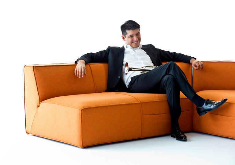 Pacho Flores sitting on a corner sofa, with his trumpet