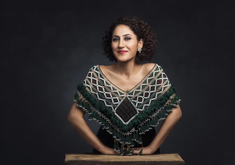 Aynur wearing an embroidered shawl leaning on a small wooden table